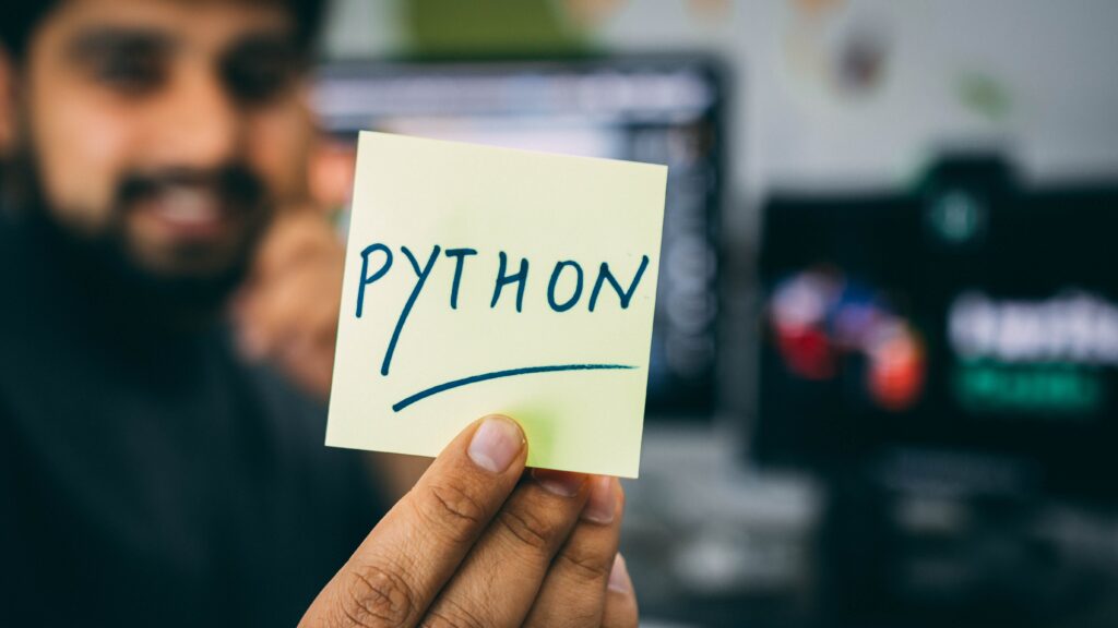 a person holding a sticky note with written python