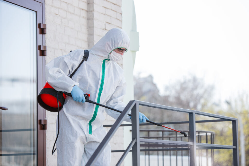 A disinfector in a protective suit and mask sprays disinfectants in the room